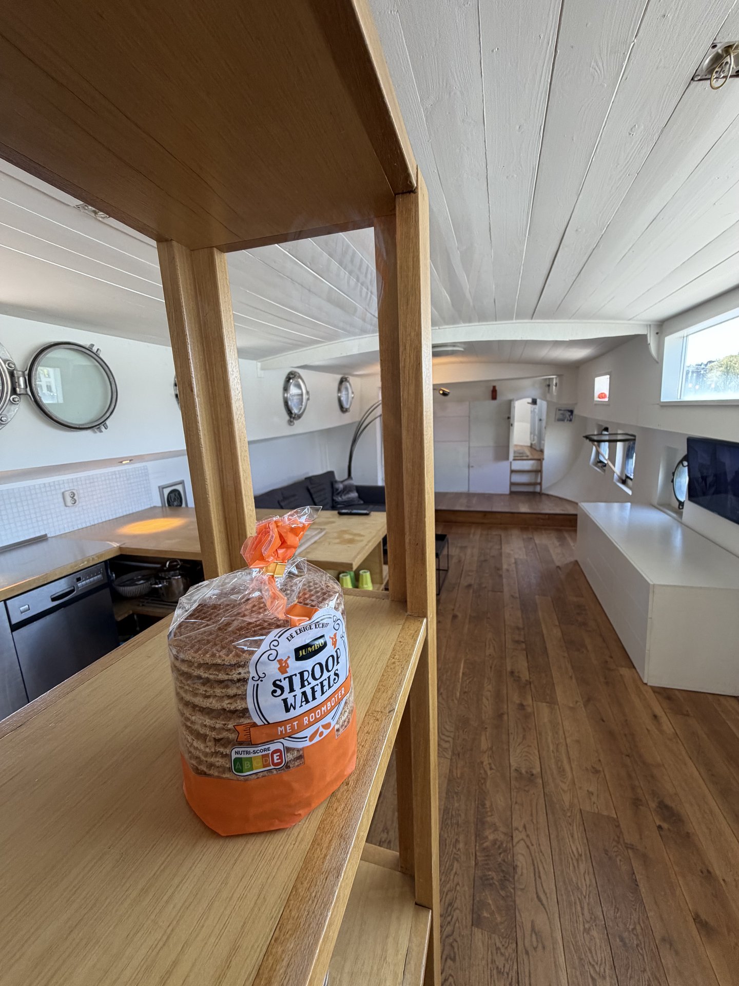 This photo captures a warm and inviting interior, likely a houseboat, with a package of Stroopwafels prominently displayed on a wooden shelf